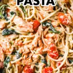 A pan with spaghetti noodles, chunks of salmon, tomatoes and spinach, all in a creamy sauce