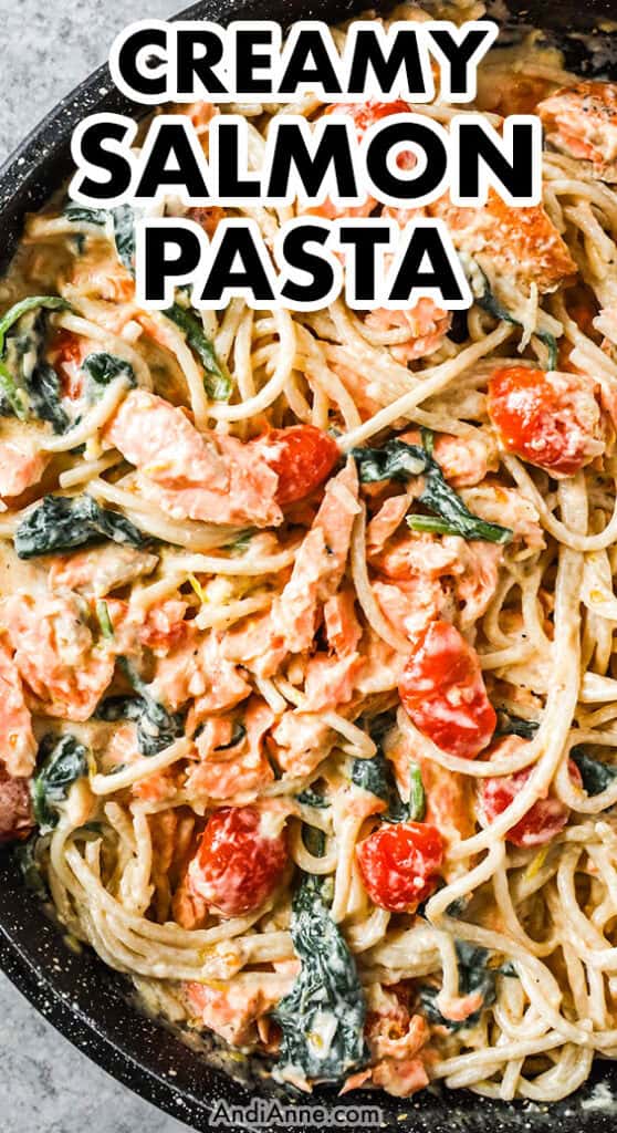 A pan with spaghetti noodles, chunks of salmon, tomatoes and spinach, all in a creamy sauce