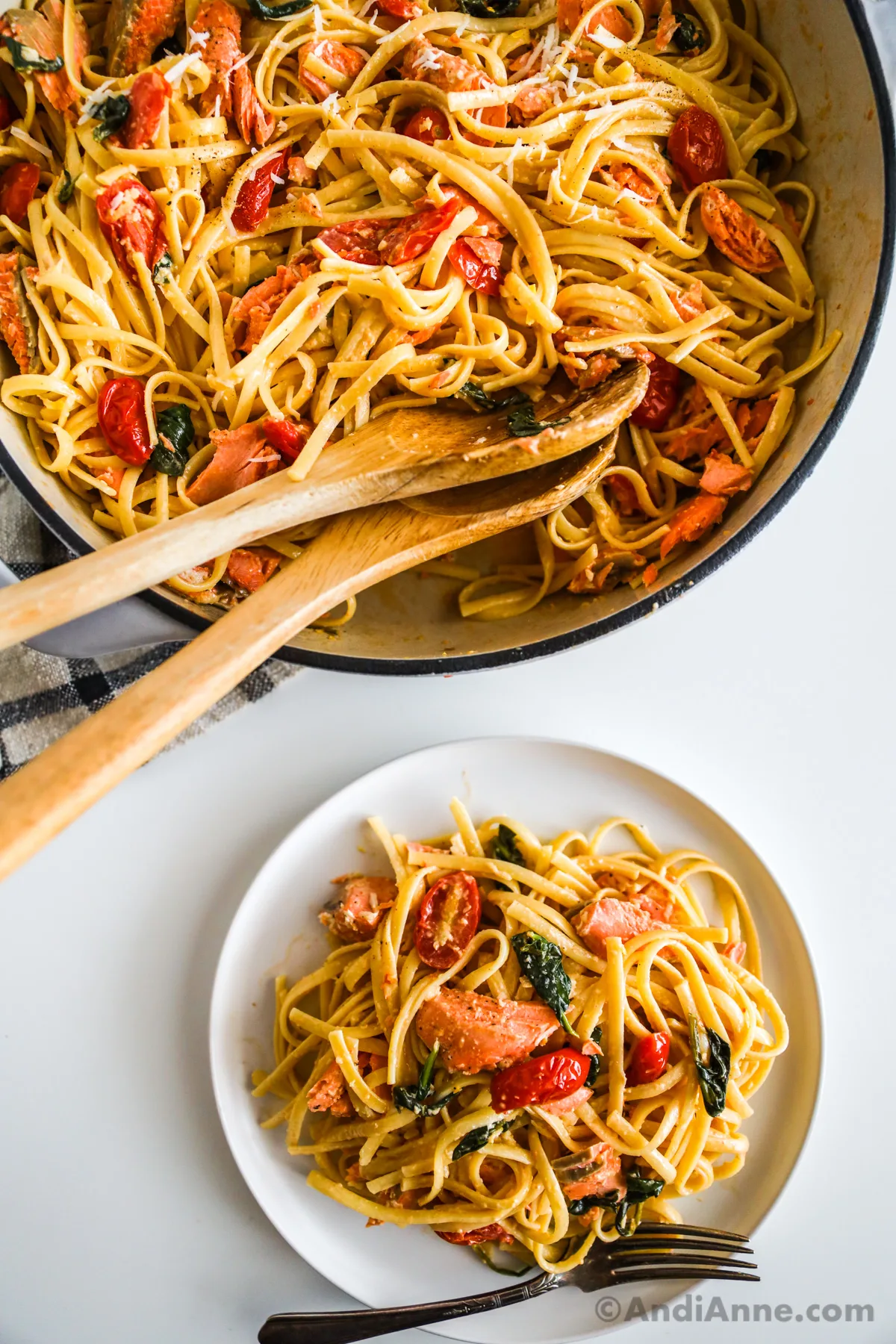 A pot of salmon pasta recipe with two wood spoons. And a white plate with the recipe and a fork.