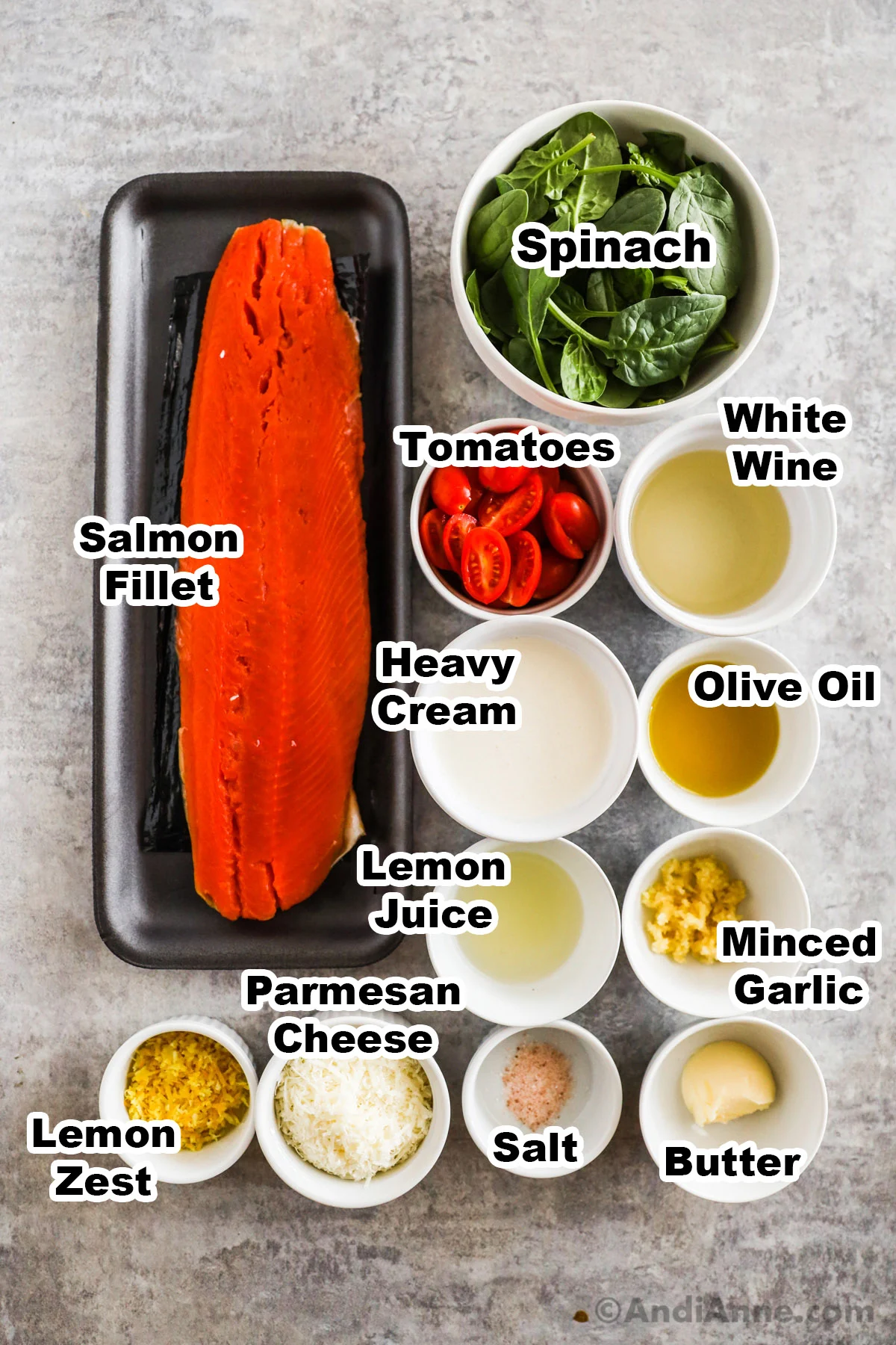 Recipe ingredients including a raw salmon fillet, and bowls of spinach, grape tomatoes, white wine, heavy cream, olive oil, lemon juice, minced garlic, lemon zest and parmesan cheese.