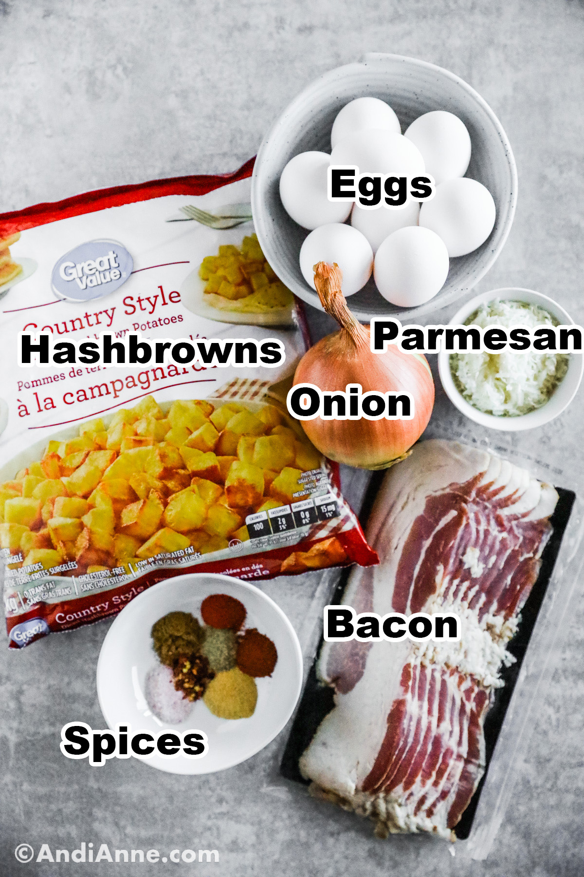 Recipe ingredients on including a bag of hash browns, bowls of eggs and grated parmesan, an onion, raw bacon and bowl of spices.