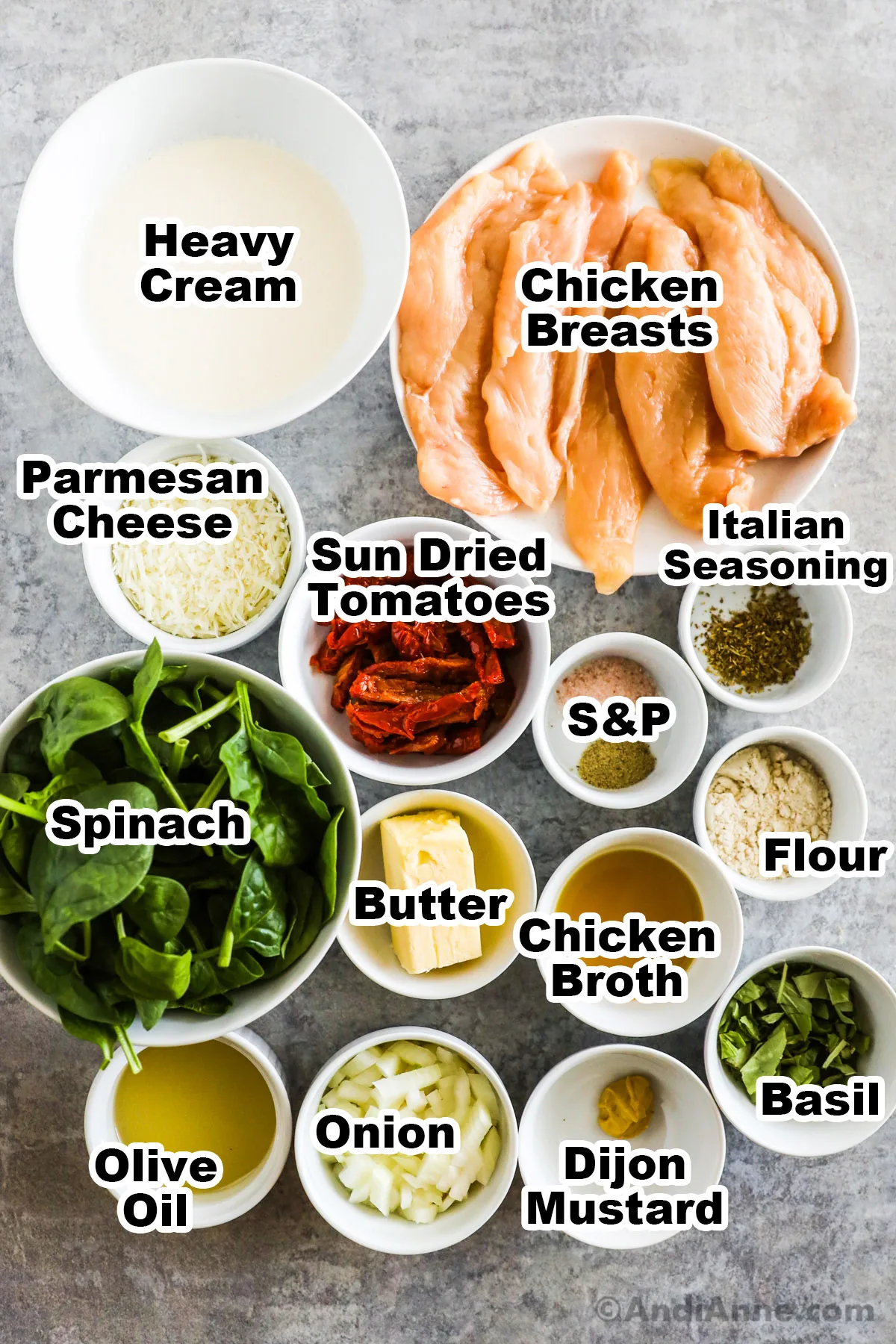 Recipe ingredients on the counter including bowl of heavy cream, sliced chicken breasts, parmesan cheese, sun dried tomatoes, spinach, spices, butter, broth, oil, and flour.