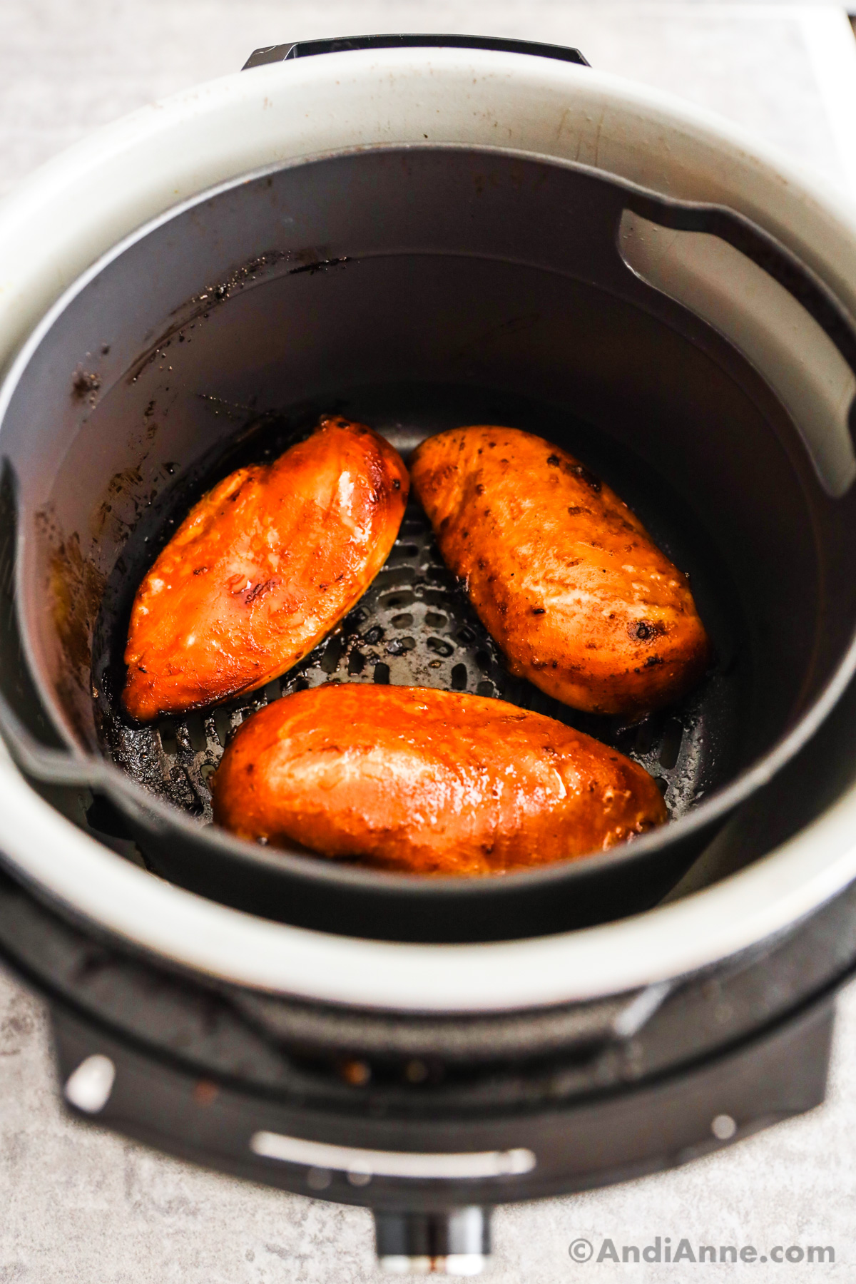 Looking into an air fryer with three cooked chicken breasts.