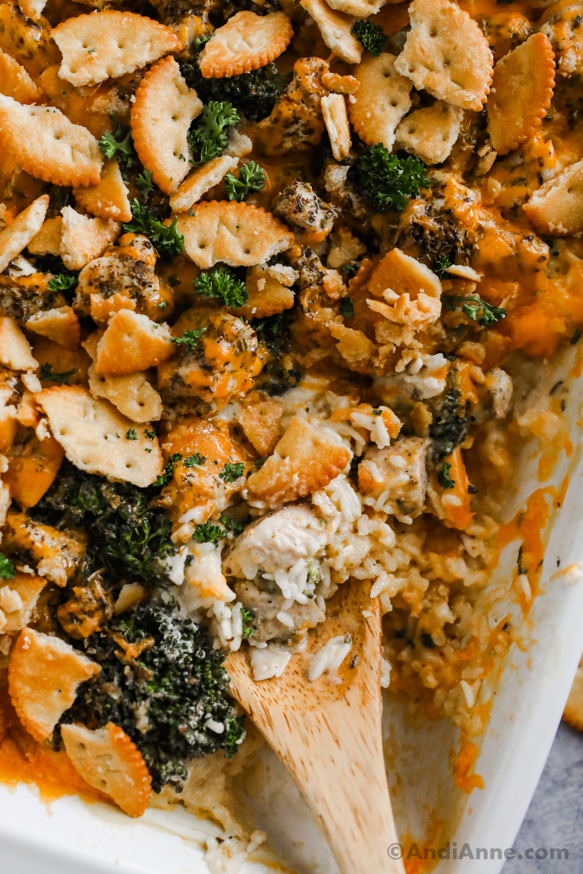 Close up of crushed crackers, chicken, rice and broccoli with a wood spoon in casserole dish.