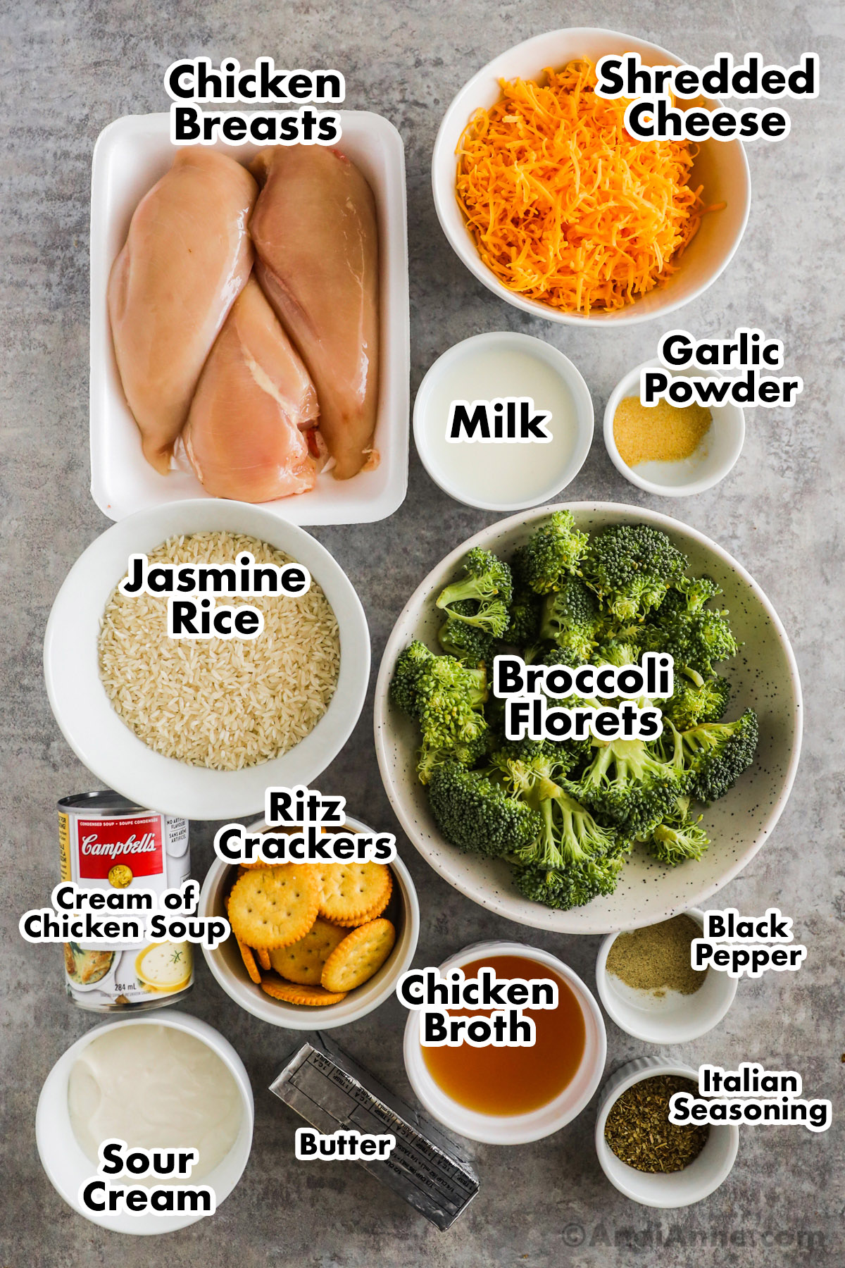 Recipe ingredients on counter. A dish of three raw chicken breasts, and bowls of shredded cheese, milk, garlic powder, jasmine rice, broccoli florets, ritz crackers ,chicken broth, sour cream, italian seasoning and can of cream of chicken soup.