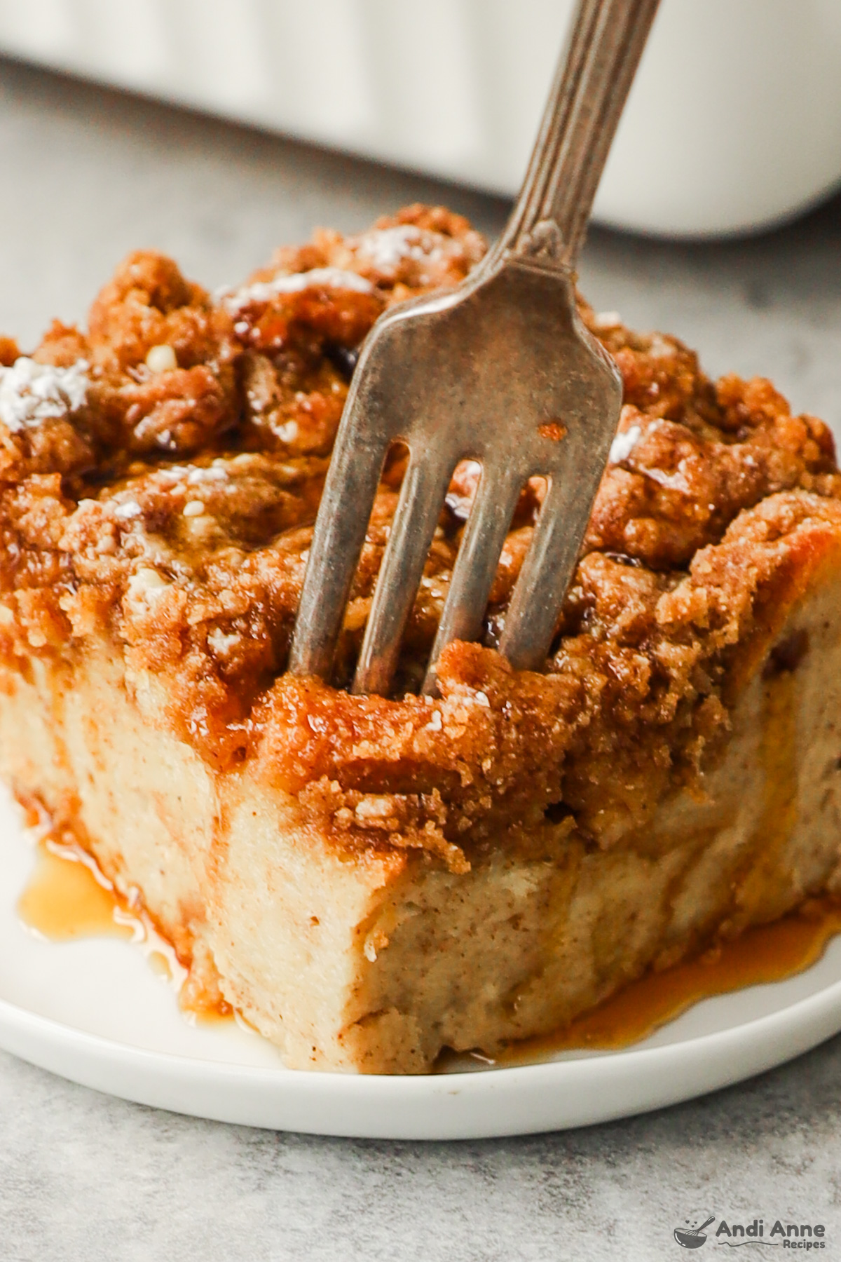 A slice of french toast bake drizzled with maple syrup and a fork digging in.