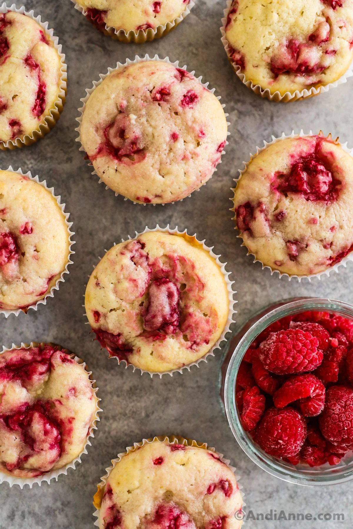 Close up of raspberry muffins with a bowl of frozen raspberries beside them.