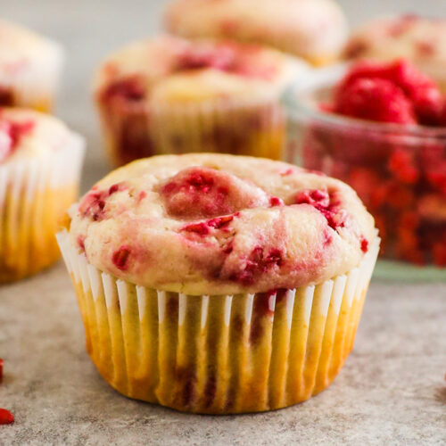 raspberry muffins with a bowl of frozen raspberries.