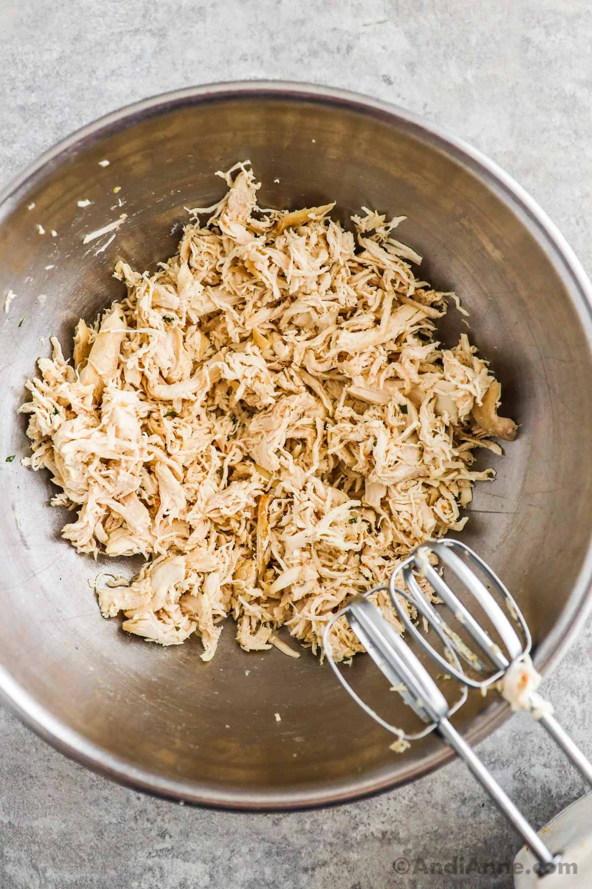 Shredded chicken in a large bowl with a hand mixer.