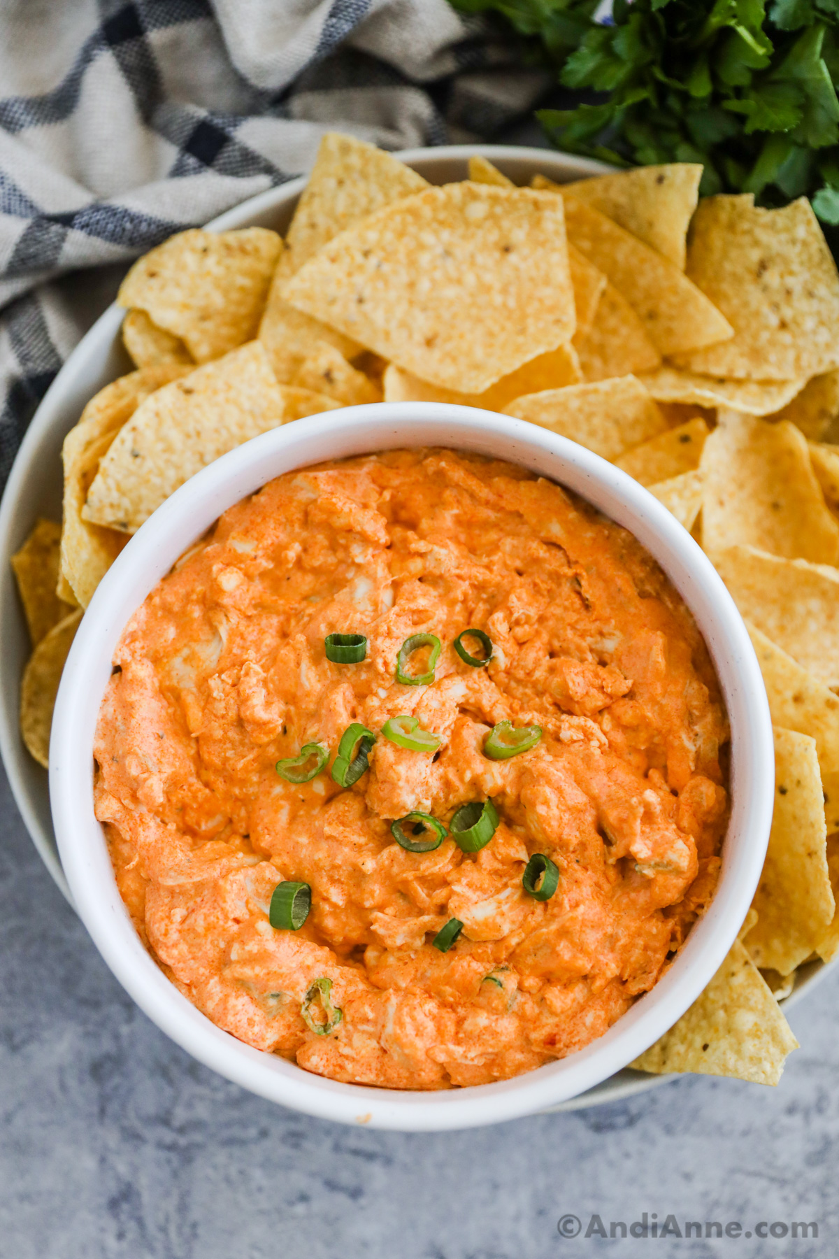 A bowl of buffalo chicken dip with tortilla chips on a plate.