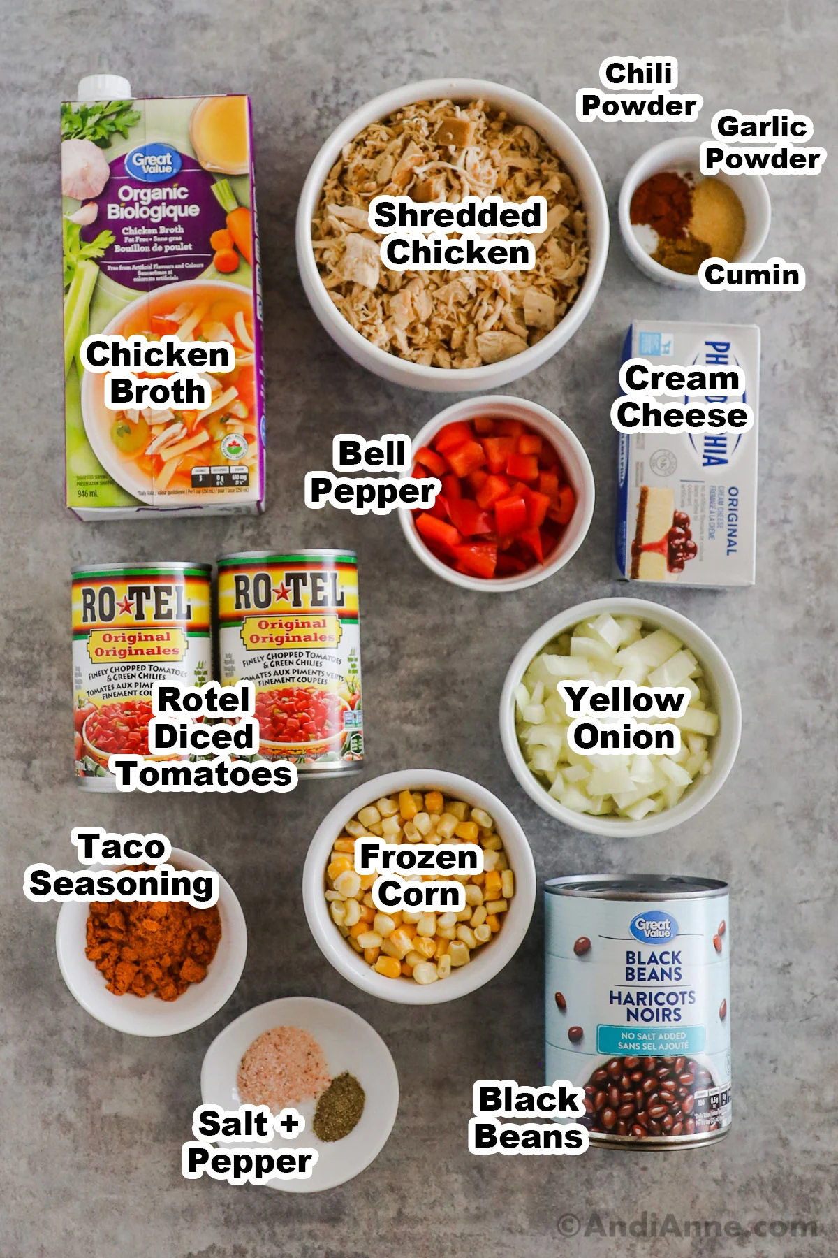 Recipe ingredients on the counter including a bowl of shredded chicken, container of chicken broth, cream cheese, chopped bell pepper, spices, chopped onion, taco seasoning, frozen corn, cans of rotel diced tomatoes with green chilies, can of black beans, salt and pepper.