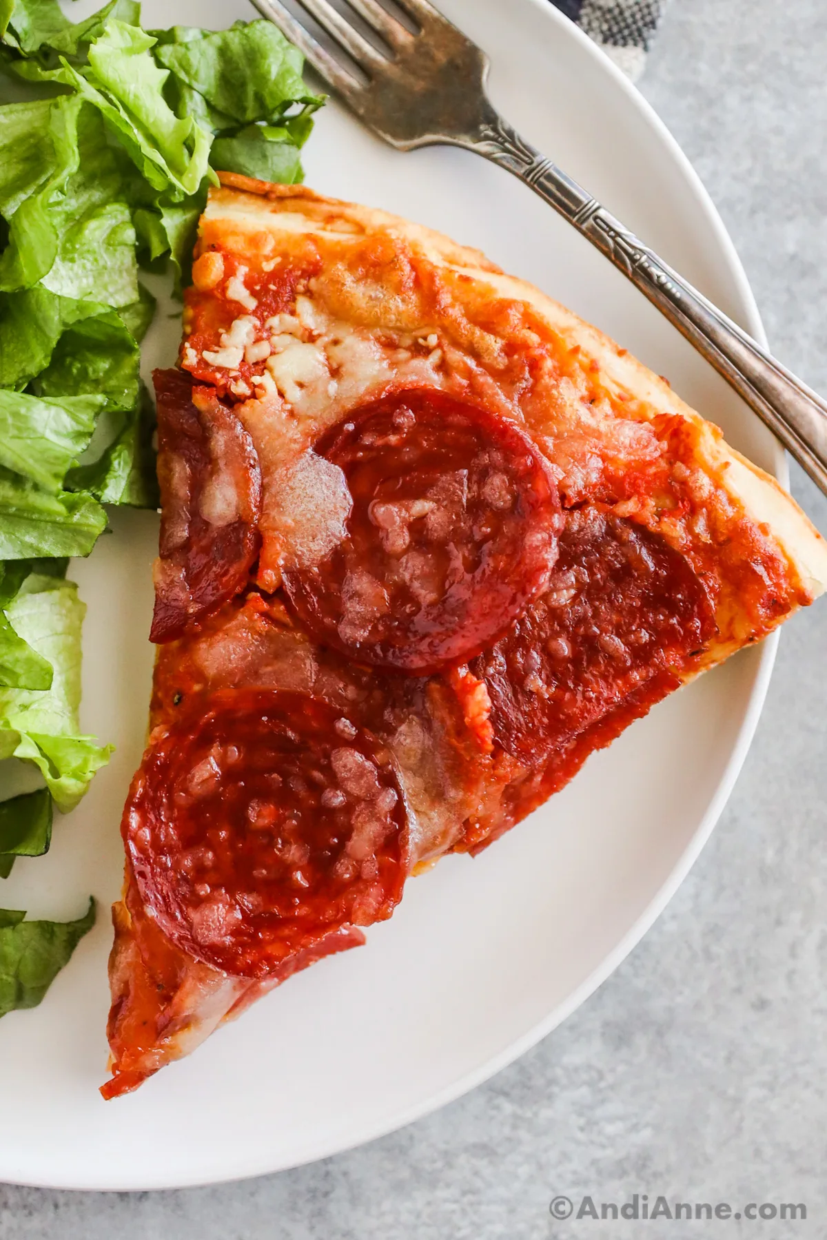 A slice of Costco pepperoni pizza with lettuce and a fork on a plate.