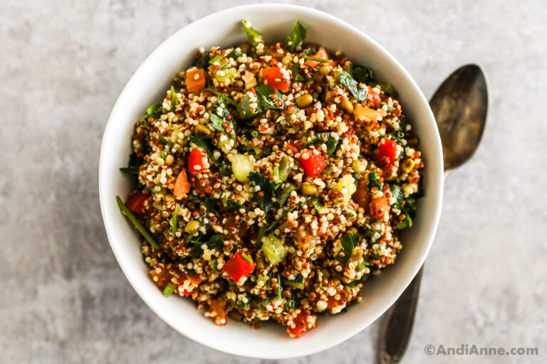 A white bowl with quinoa salad and a spoon.