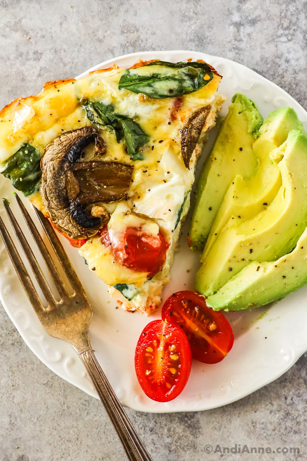 A slice of vegetable quiche, with slices of avocado, grape tomato and a fork
