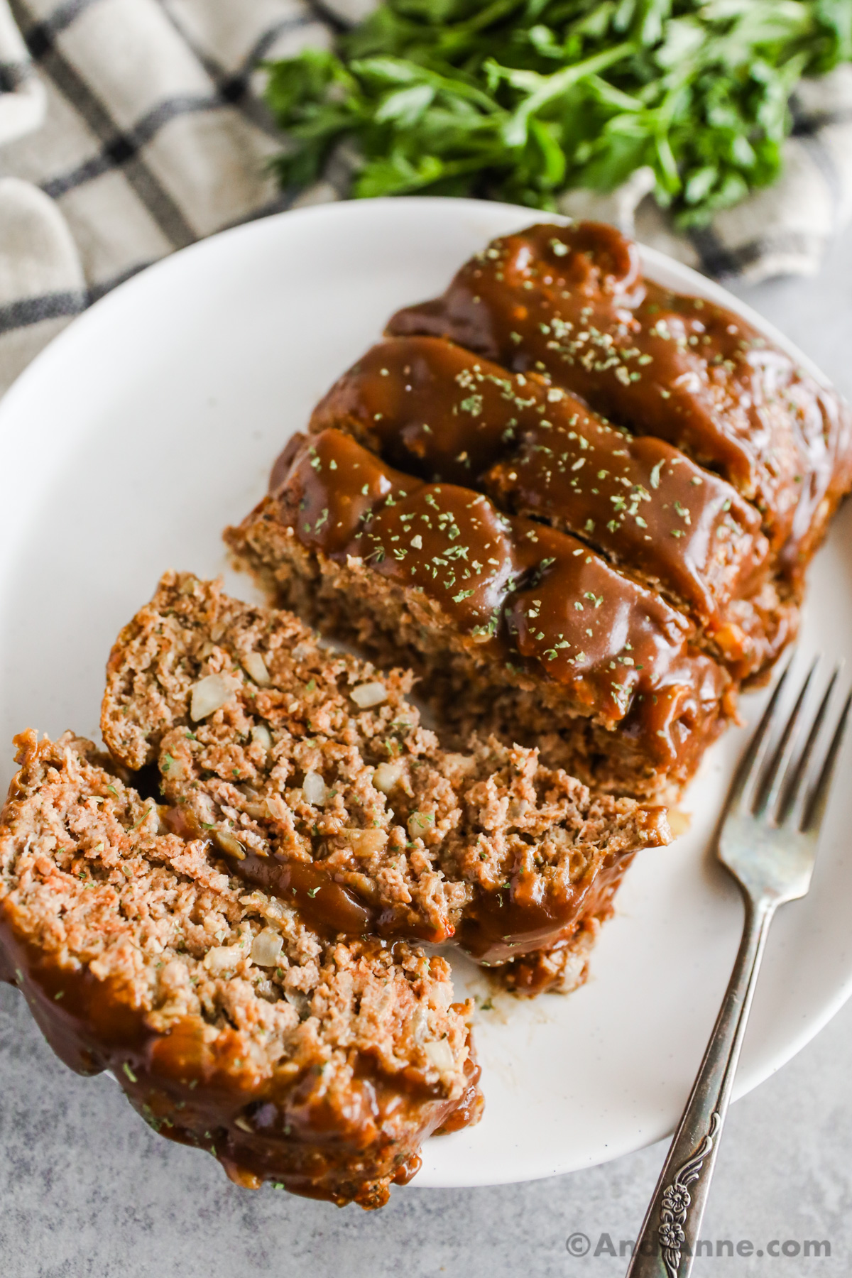 Sliced meatloaf with brown gravy topping and a fork on a white plate.