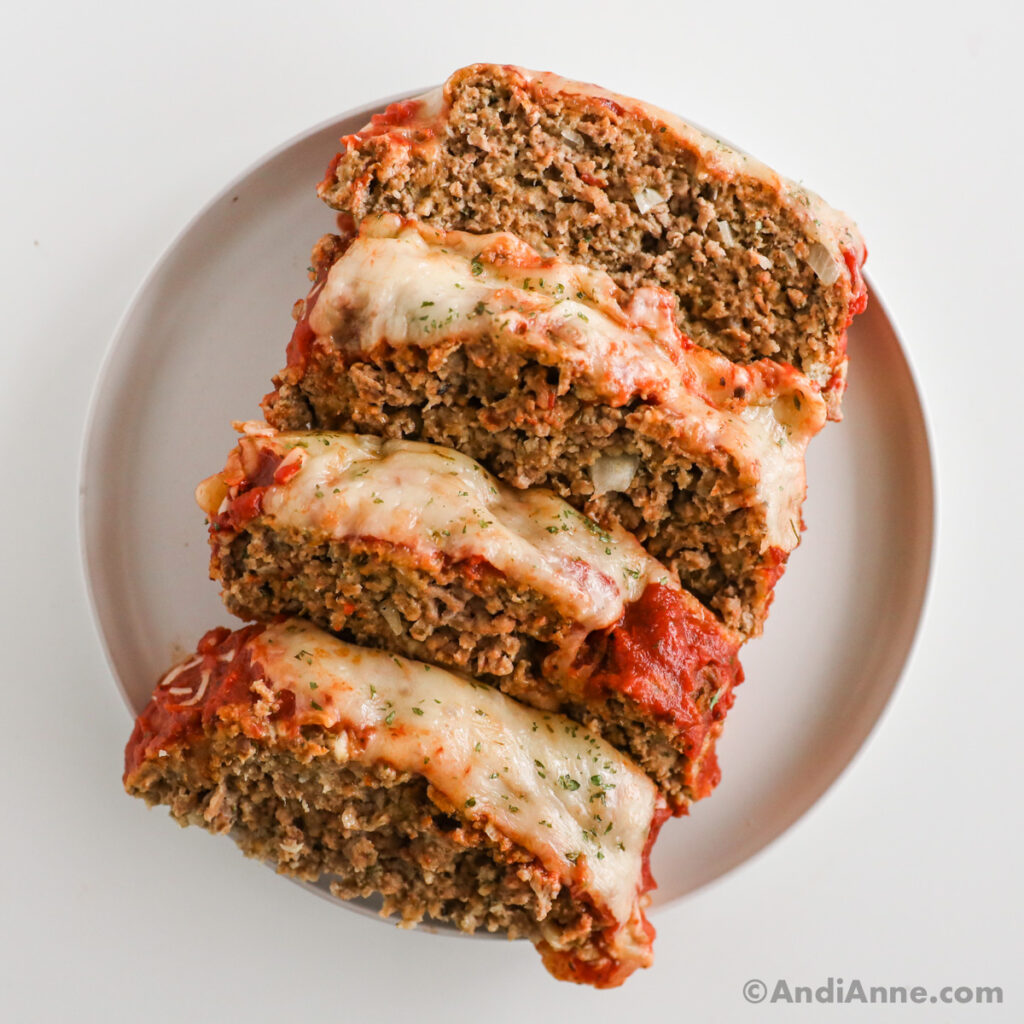 Sliced Italian meatloaf recipe topped with spaghetti sauce and melted cheese on a white plate.
