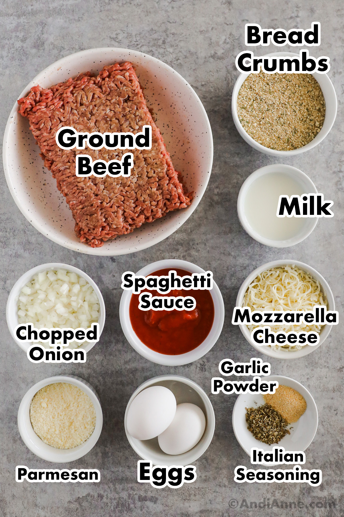 Recipe ingredients on the counter including raw ground beef, bowls of bread crumbs, milk, mozzarella cheese, spaghetti sauce, chopped onion, parmesan and eggs.