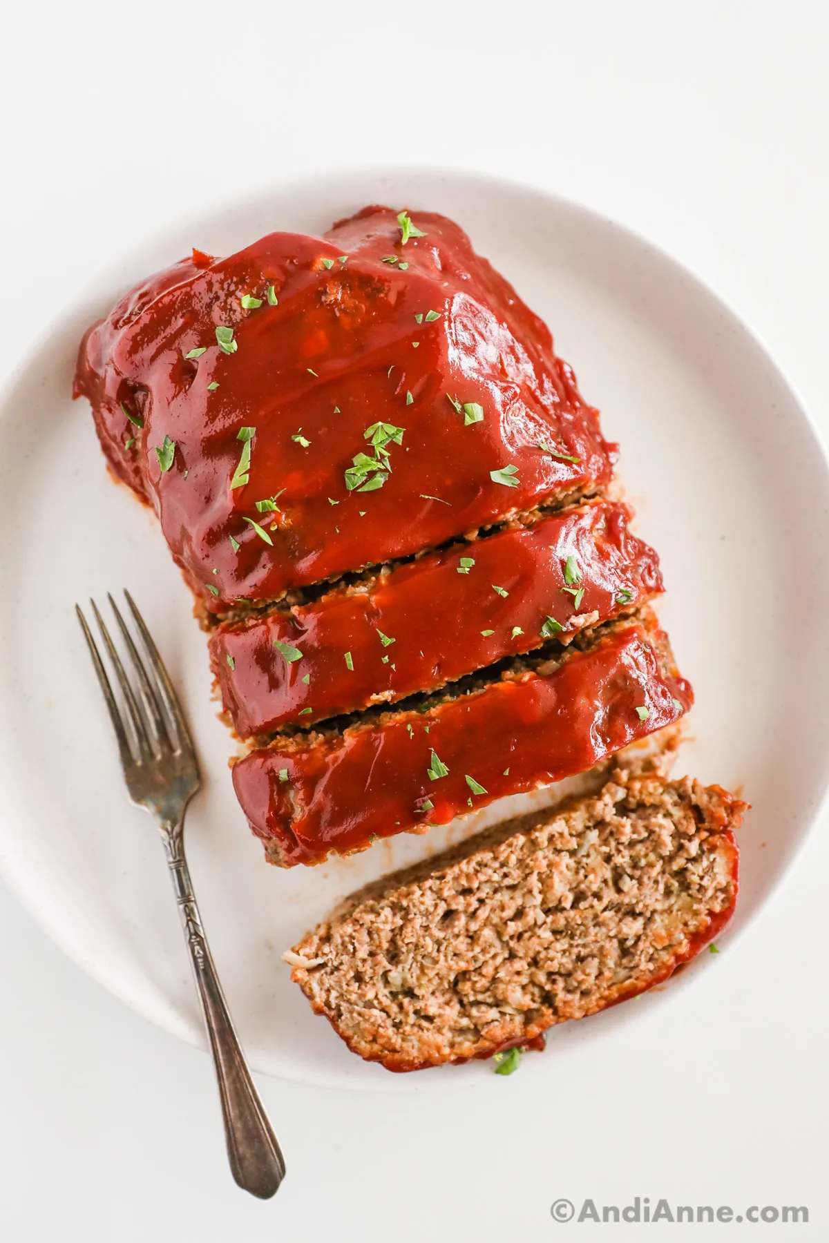 Classic meatloaf sliced and on a white plate with a fork.