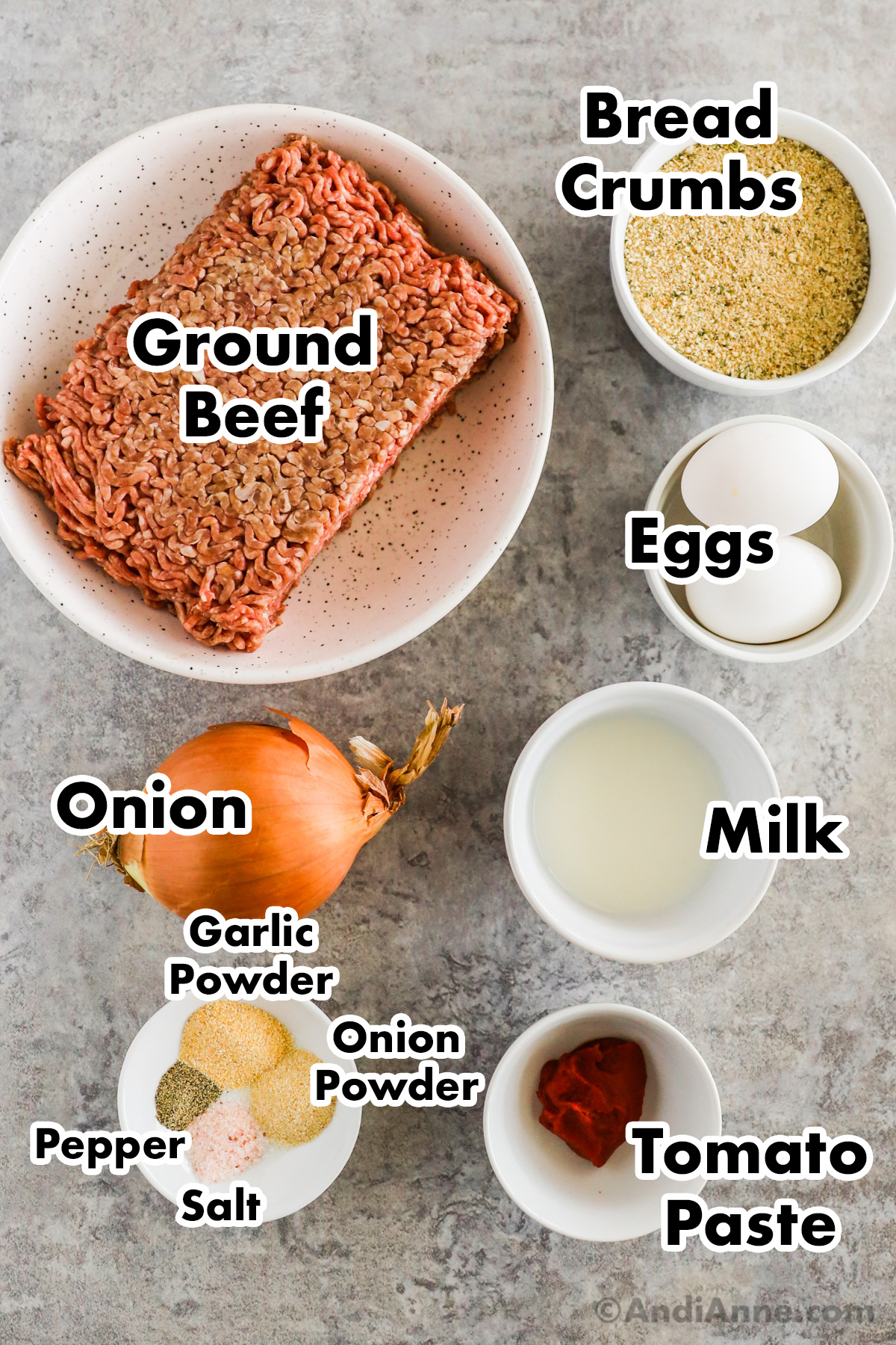 Recipe ingredients on a counter including raw ground beef, bowl of bread crumbs, eggs, milk, onion, spices and tomato paste.