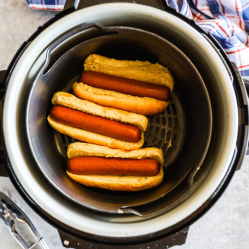 Looking into an air fryer with 3 hot dogs and buns.
