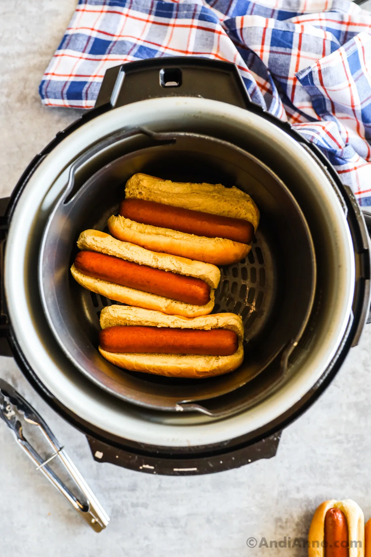 Looking into an air fryer with three hot dogs with buns.
