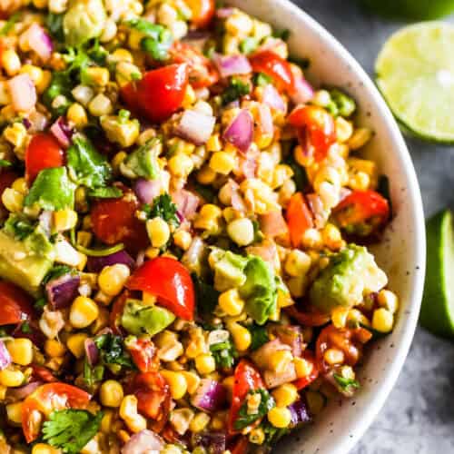 A white bowl of avocado corn salad with tomatoes and cilantro.