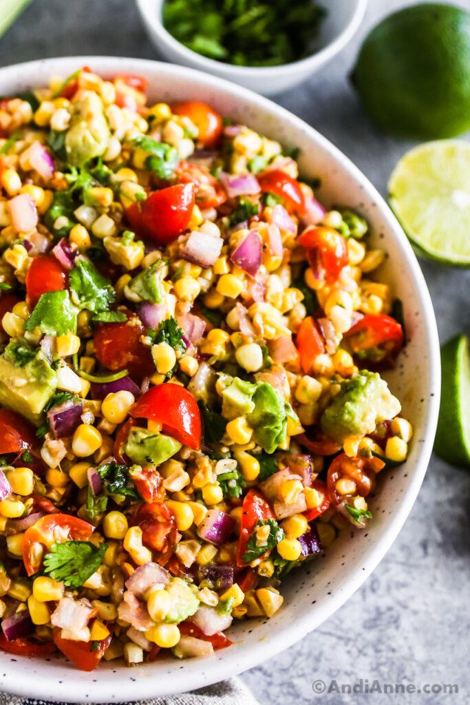 A white bowl of avocado corn salad with tomatoes and cilantro.