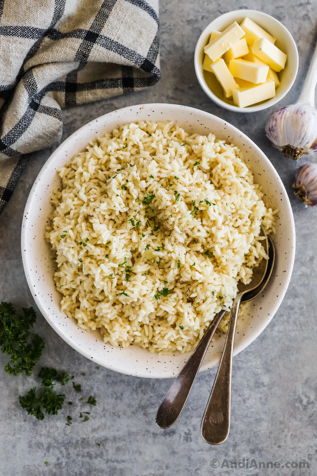 A white bowl with garlic butter rice and two spoons.