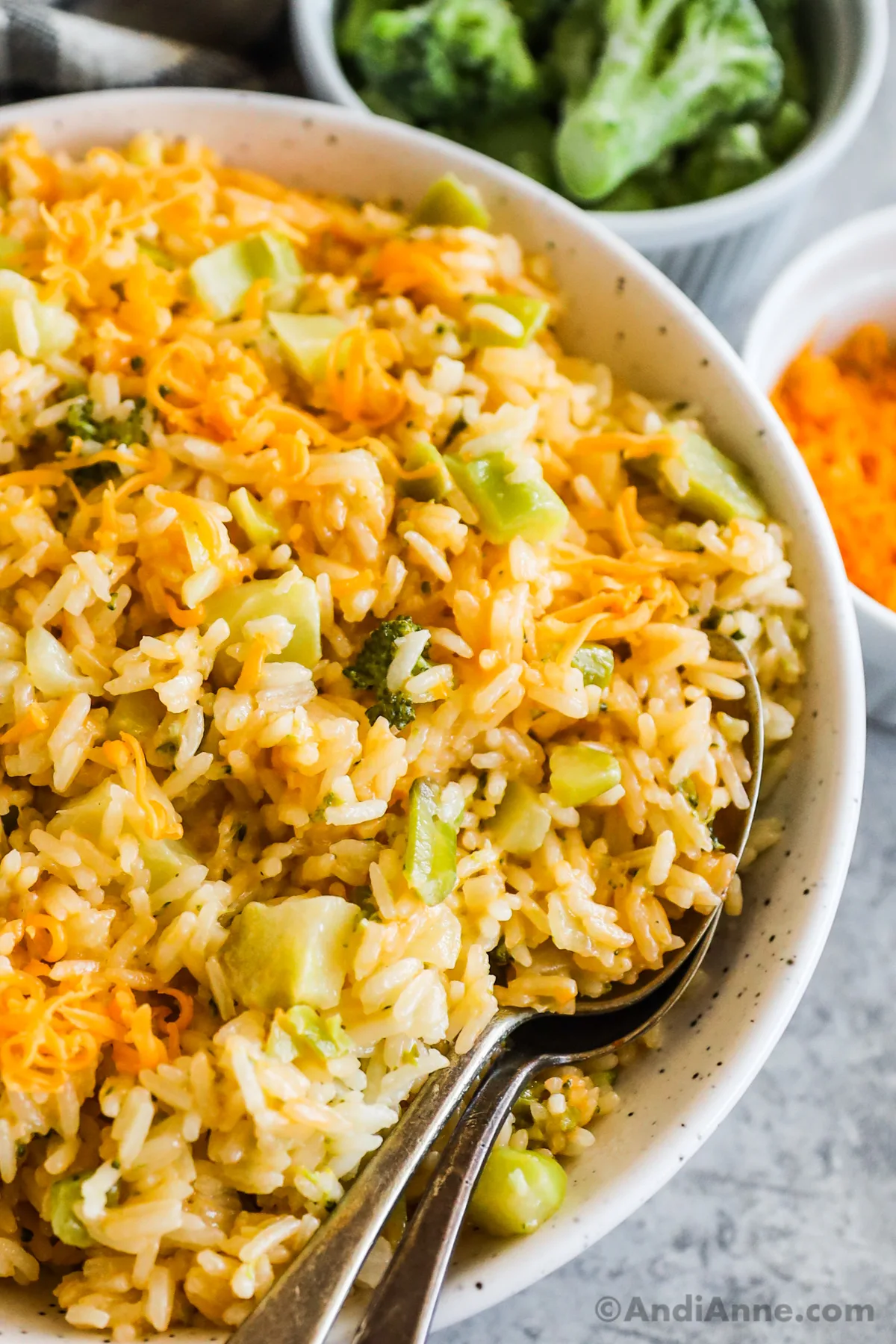 A bowl with cheddar broccoli rice and two spoons.