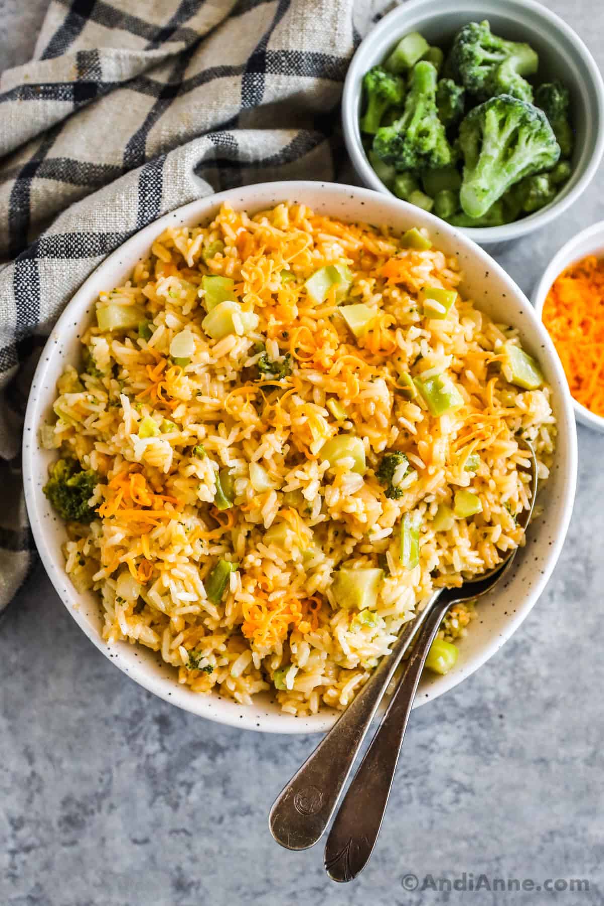 A white bowl with broccoli cheddar rice and two spoons.