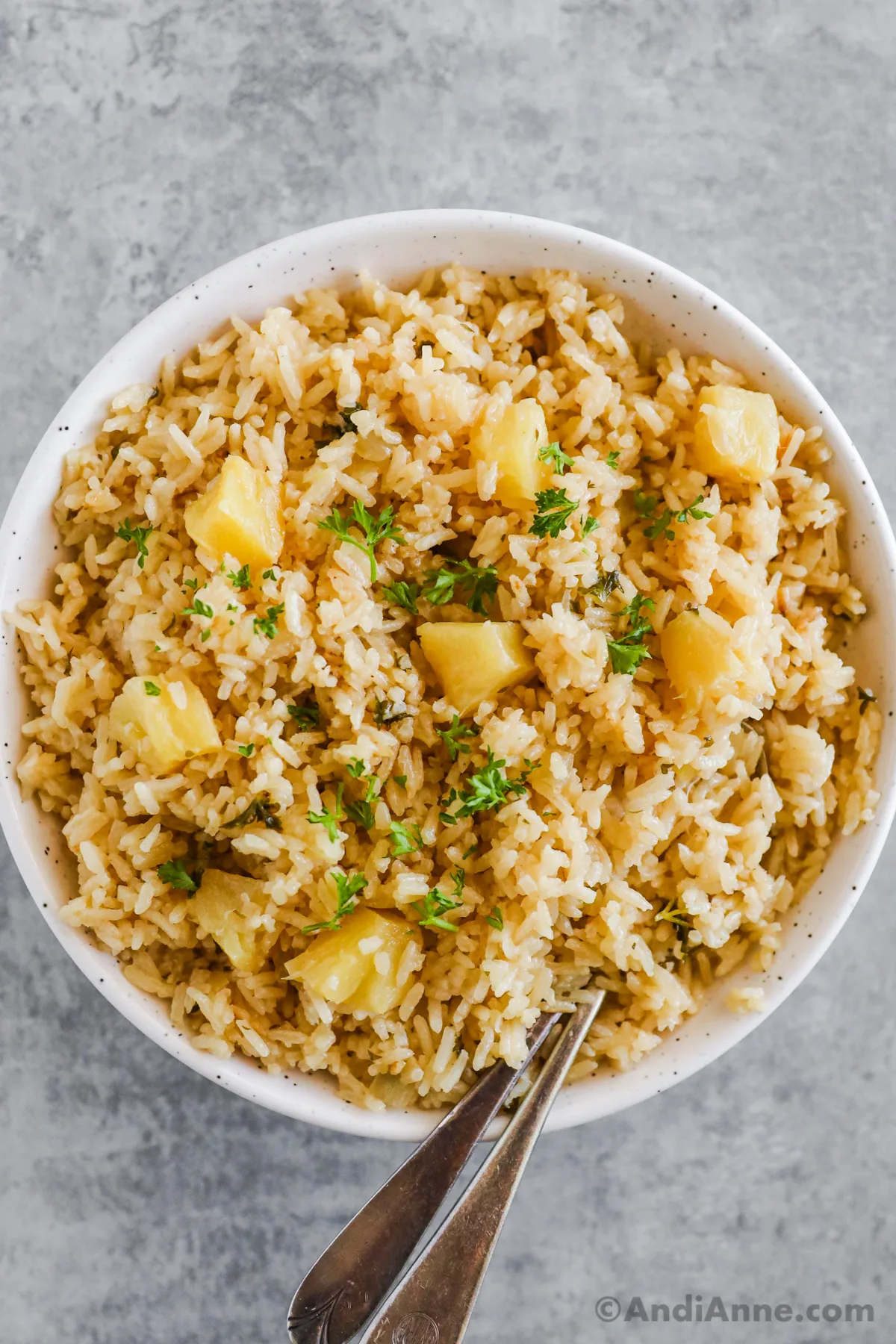 A white bowl with coconut pineapple rice with chopped parsley and pineapple chunks.