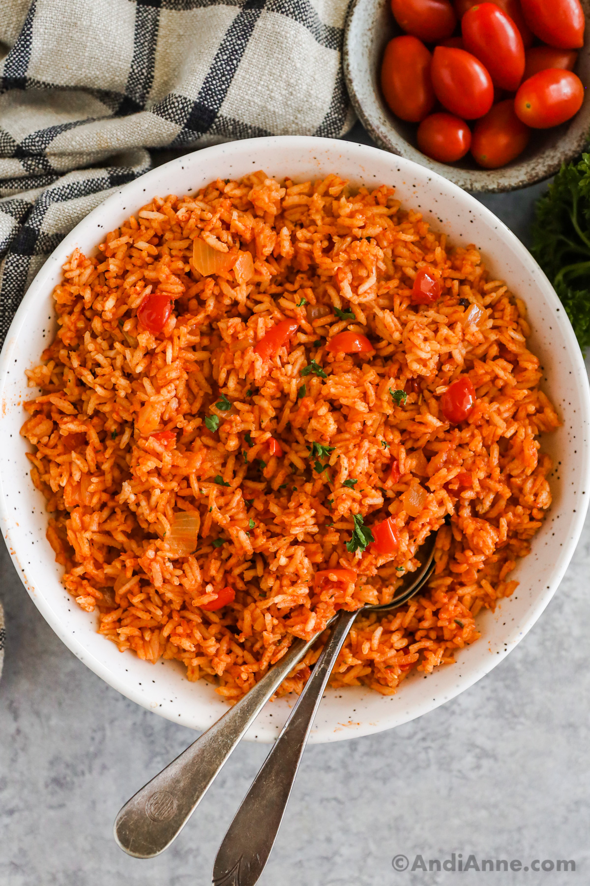 A white bowl with red colored spanish rice and two spoons. 