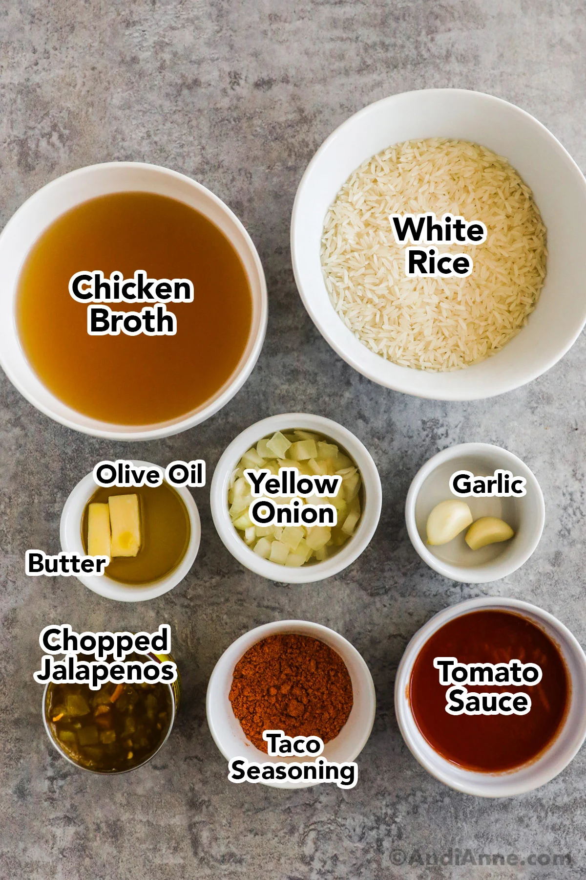 Recipe ingredients including bowls of chicken broth, jasmine rice, olive oil and butter, yellow onion, garlic cloves, canned chopped jalapenos, taco seasoning spice and tomato sauce.