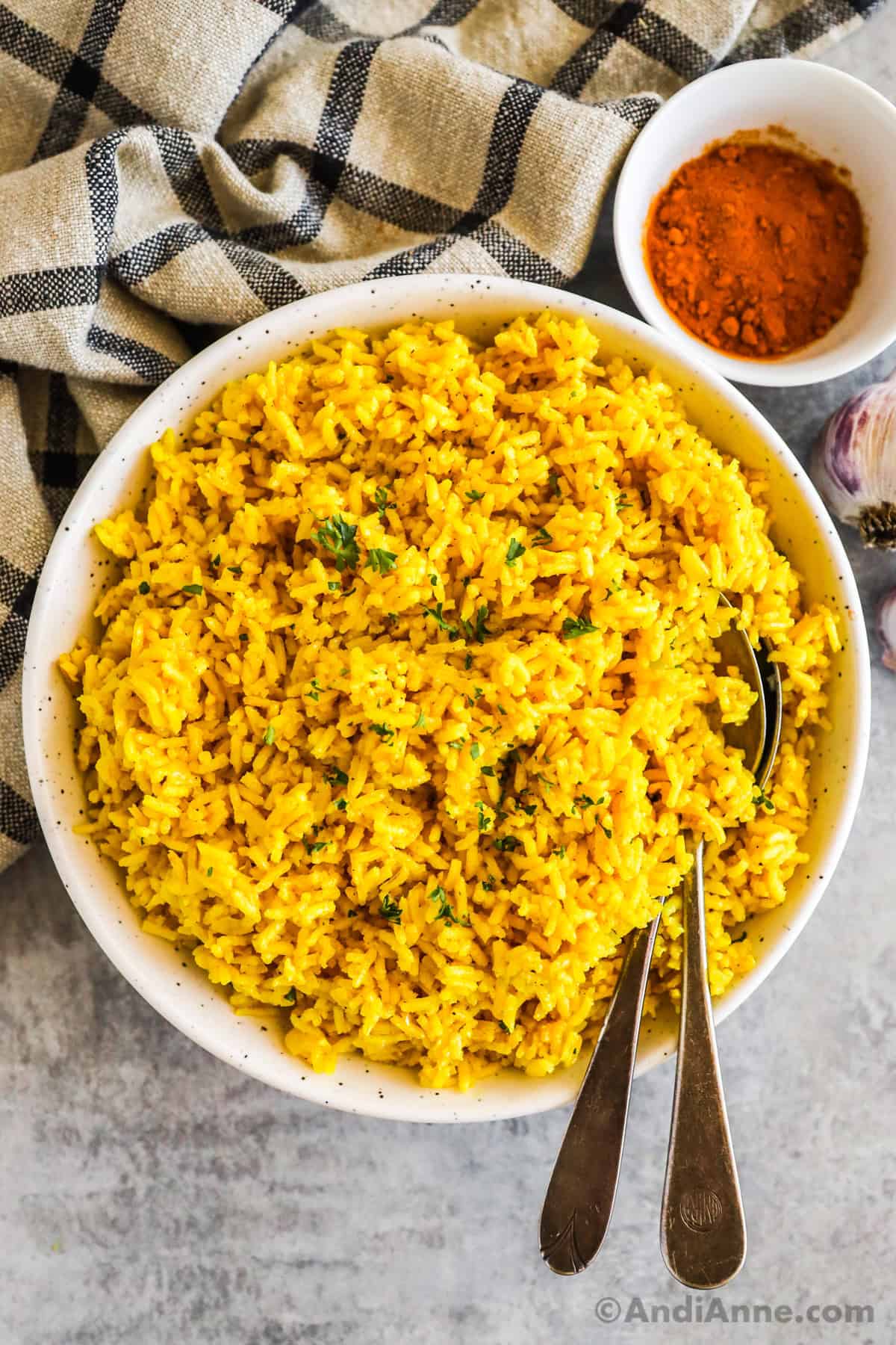 A white bowl of turmeric rice with spoons and a small bowl of turmeric powder.