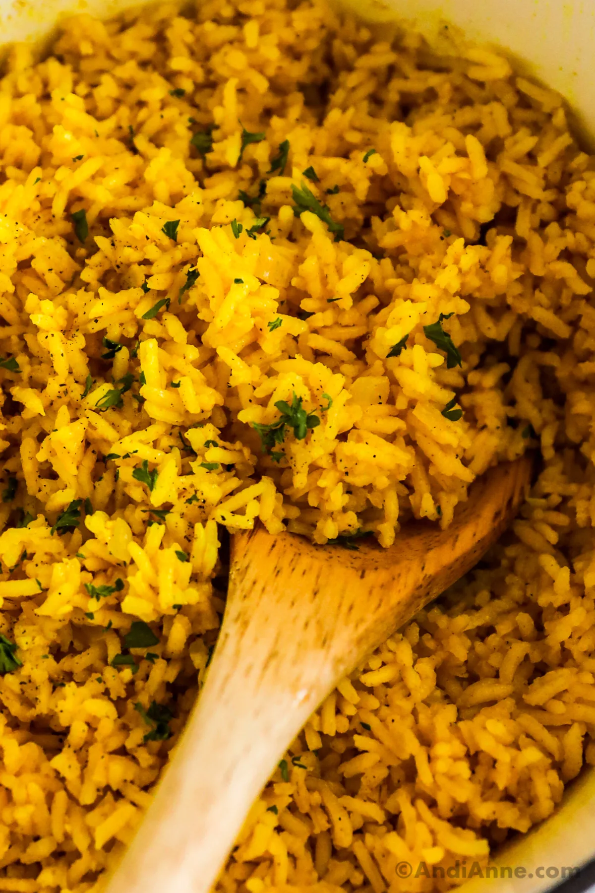 Detail photo of yellow turmeric rice with a wood spoon and bits of chopped parsley.
