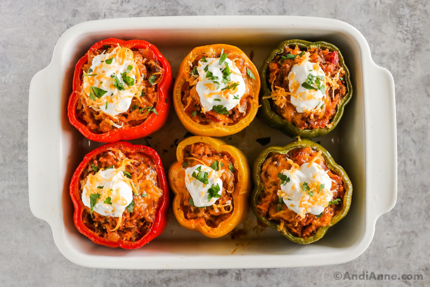 Sour cream on top of cooked stuffed bell peppers in a baking dish.