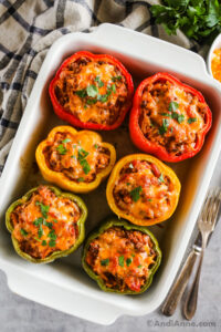 A white baking dish with six baked stuffed peppers topped with melted cheese.