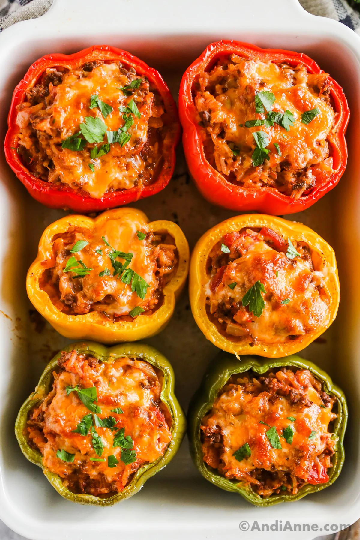 Close up of six green, yellow and red stuffed bell peppers in a baking dish topped with melted cheese.