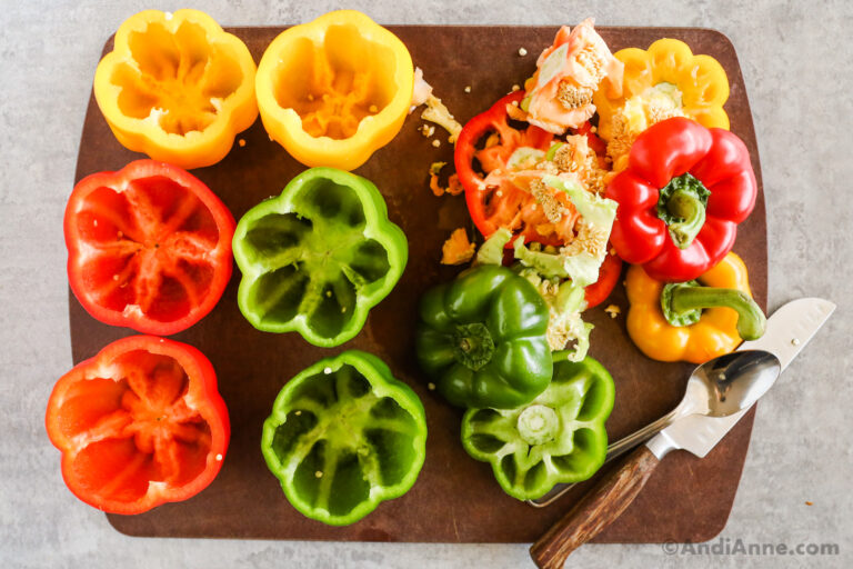 Six bell peppers with tops cut off on a cutting board with knife and pepper discards beside it.