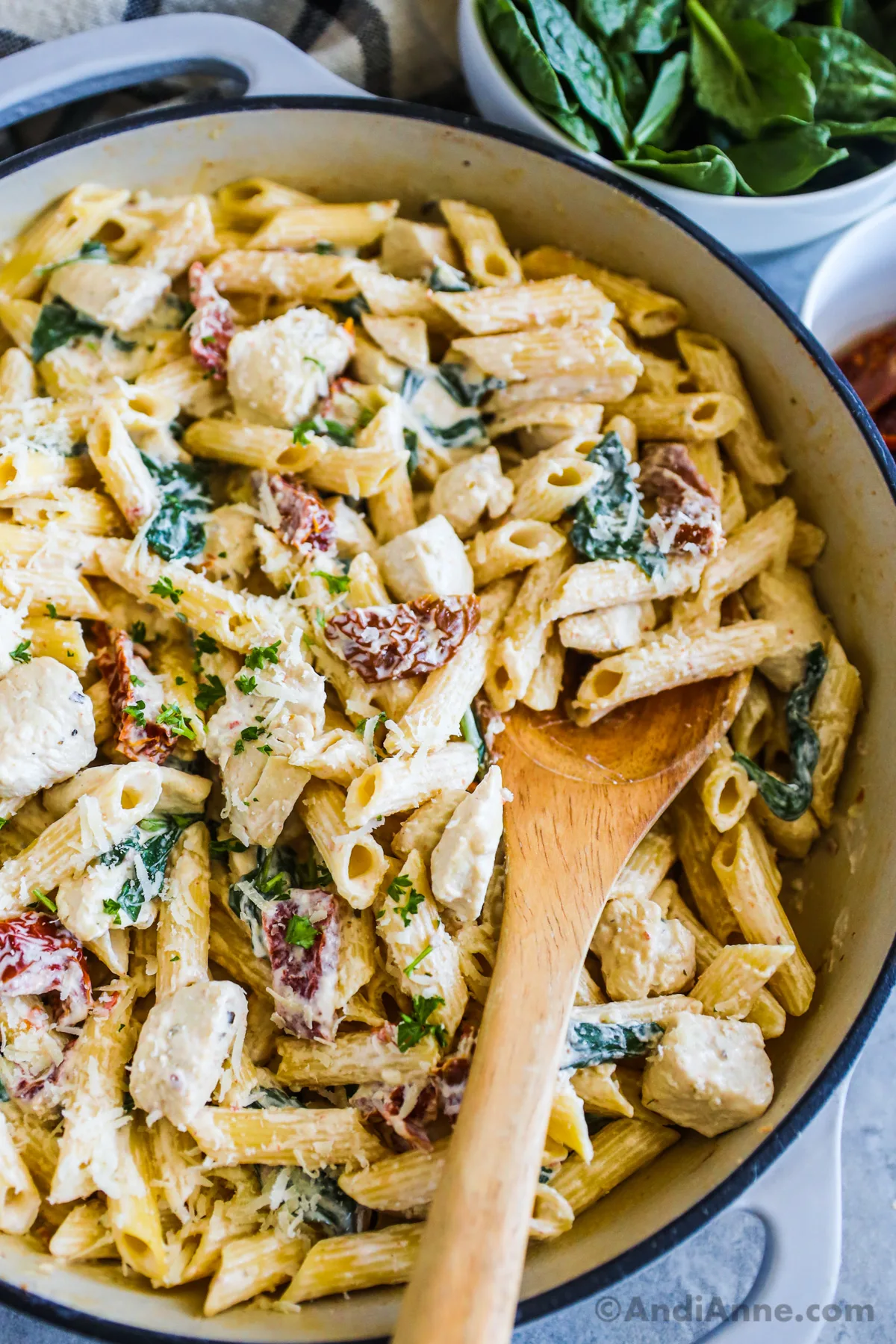 A pot of tuscan chicken pasta recipe with a wood spoon.