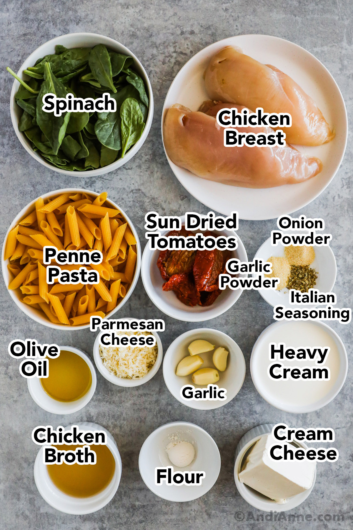 Recipe ingredients in bowls including spinach, two raw chicken breasts, uncooked penne pasta, sun dried tomatoes, parmesan cheese, cream, broth, cream cheese and garlic cloves. 