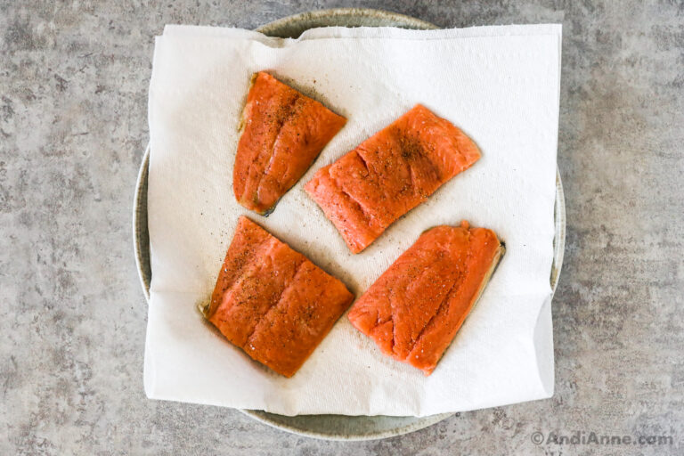 Four small uncooked salmon fillets on a paper towel.