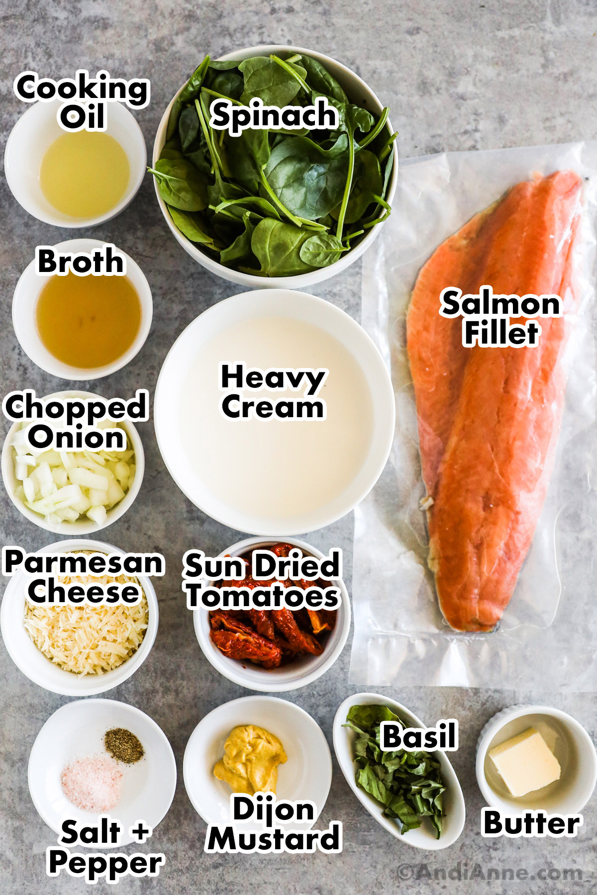 Recipe ingredients in bowls including cooking oil, spinach, broth, heavy cream, chopped onion, parmesan, sun dried tomatoes, dijon mustard, basil, butter, and a salmon fillet in plastic.