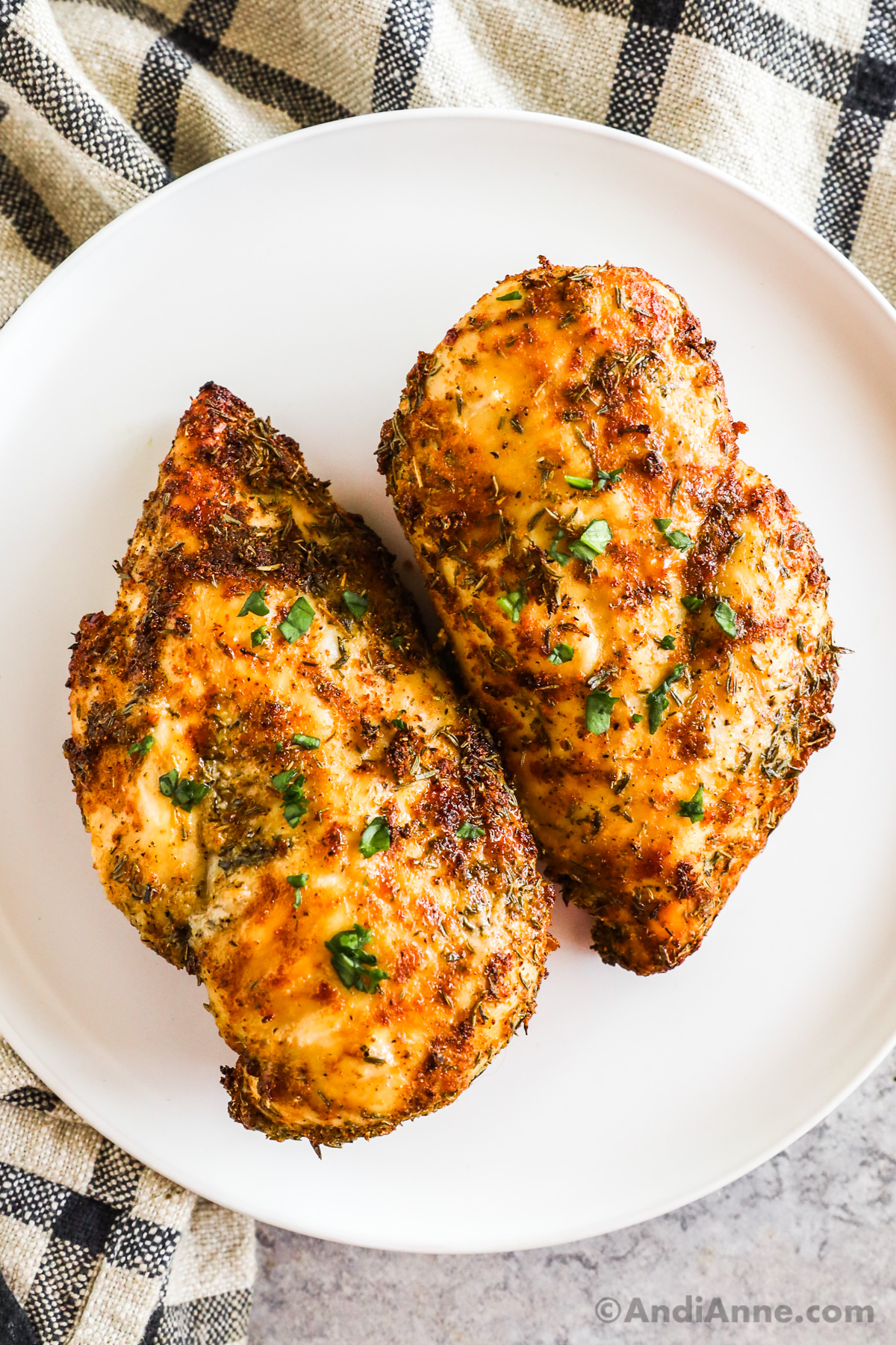 Two crispy chicken breasts with lots of seasonings sitting on a white plate that were cooked in an air fryer.