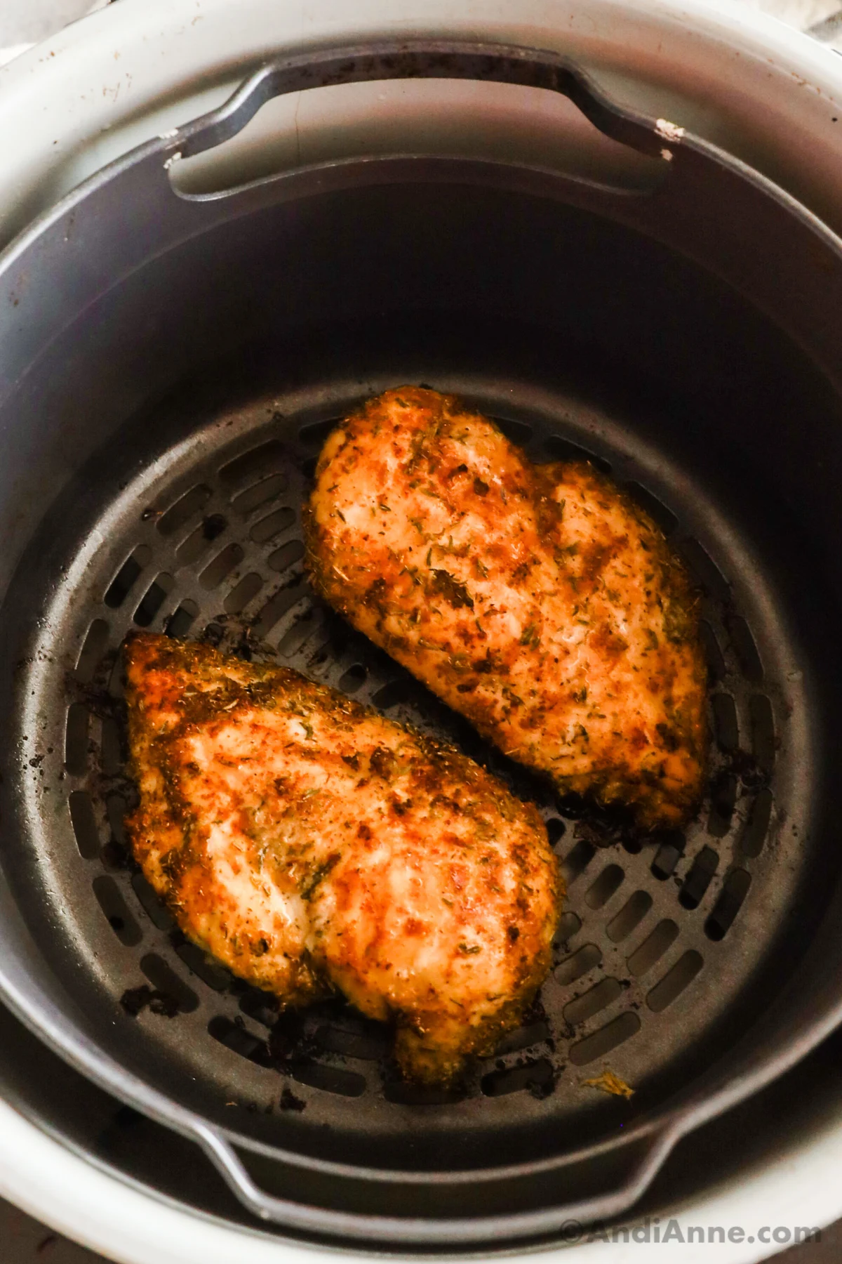 Looking into an air fryer with two cooked chicken breasts.