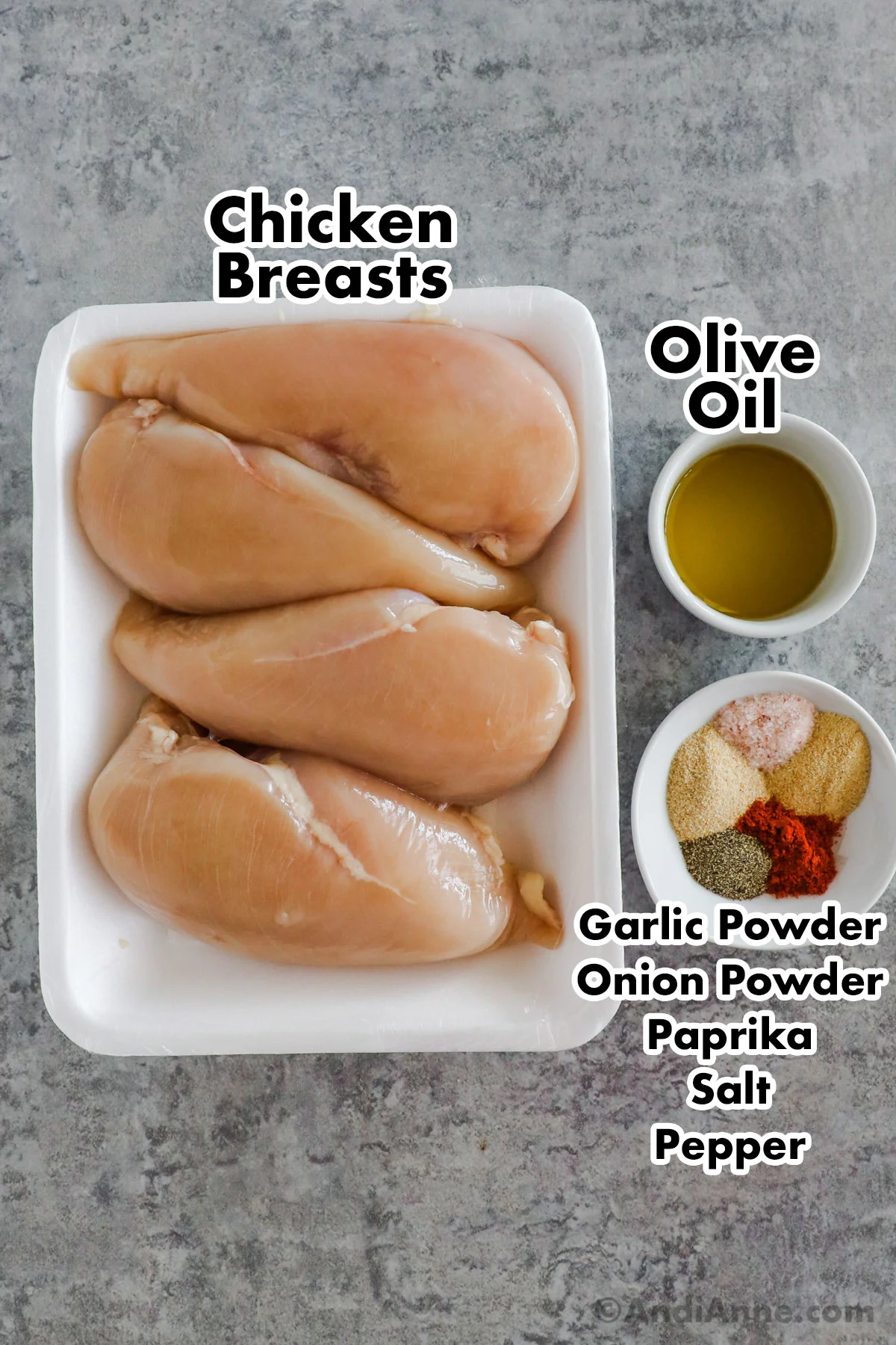 Recipe ingredients on the counter including a tray of four raw chicken breasts, a bowl of olive oil, and bowl of various spices.