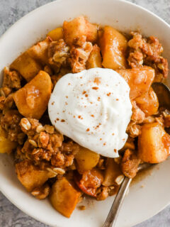A plate of apple crisp topped with a dollop of whipped cream