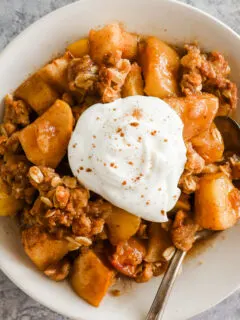 A plate of apple crisp topped with a dollop of whipped cream
