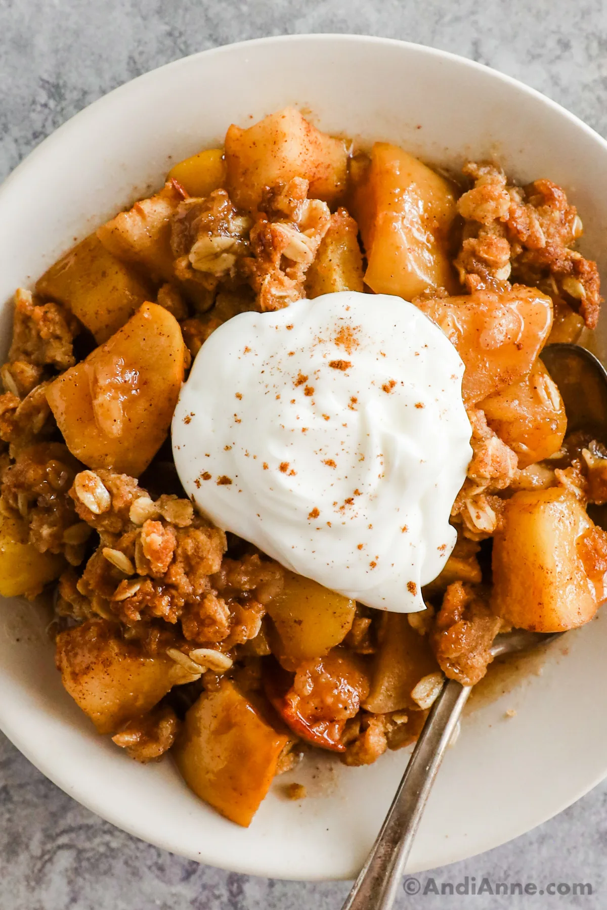 Apple crisp on a white plate with a dollop of cream in the center.