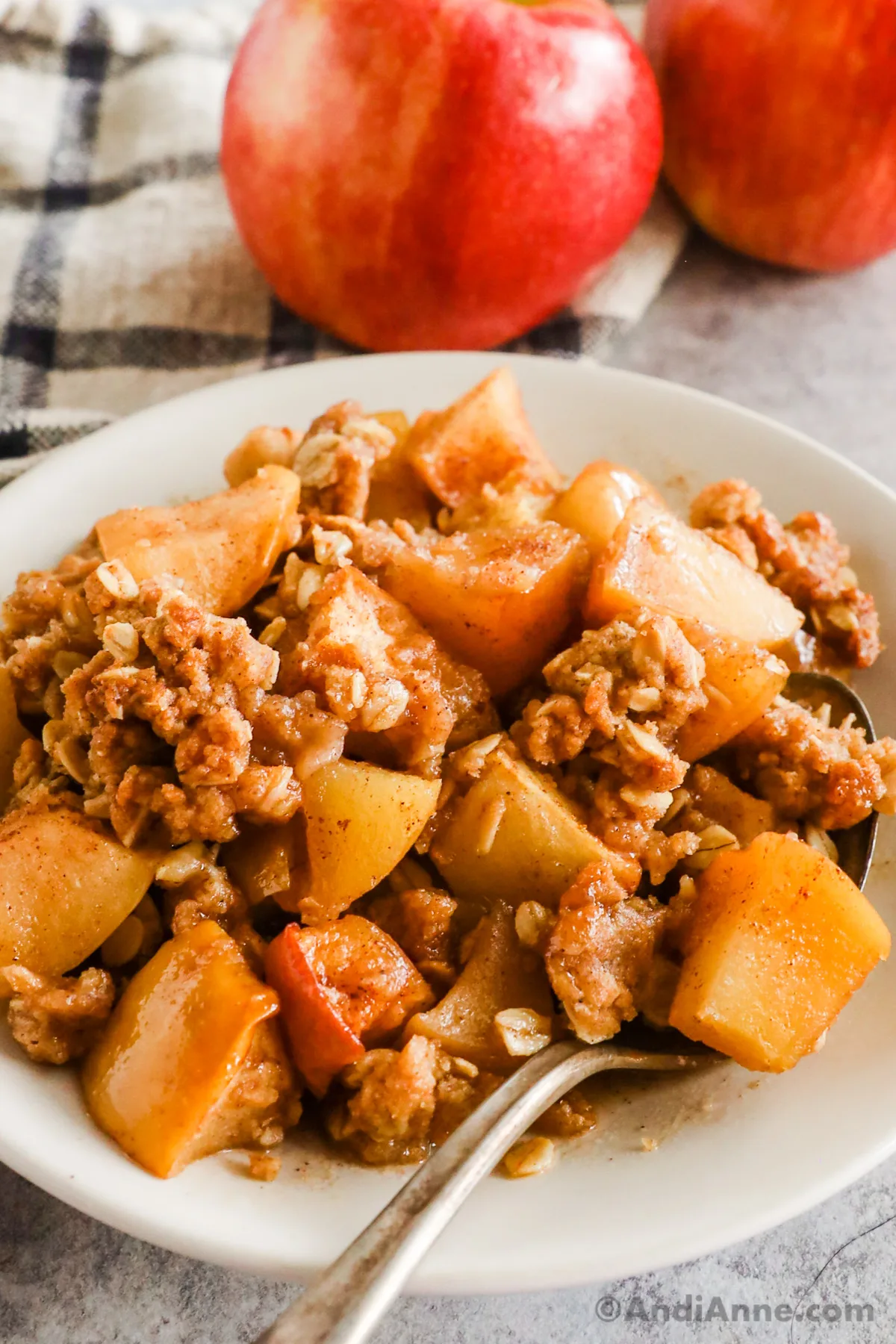 Close up of apple crisp with a spoon and two apples in the background.
